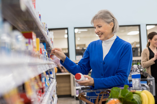Confident active senior woman shops in a grocery store pharmacy. She is looking at vitamins.