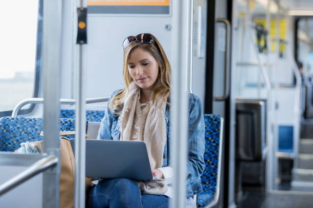 Woman works on laptop while riding commuter train A serious mid adult woman sits on a commuter train and looks down in concentration at her laptop. commuter train photos stock pictures, royalty-free photos & images