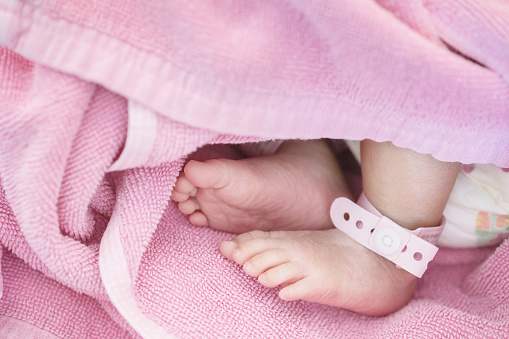 Closeup foot of baby with newborn ankle tag on bed in hospital textured background
