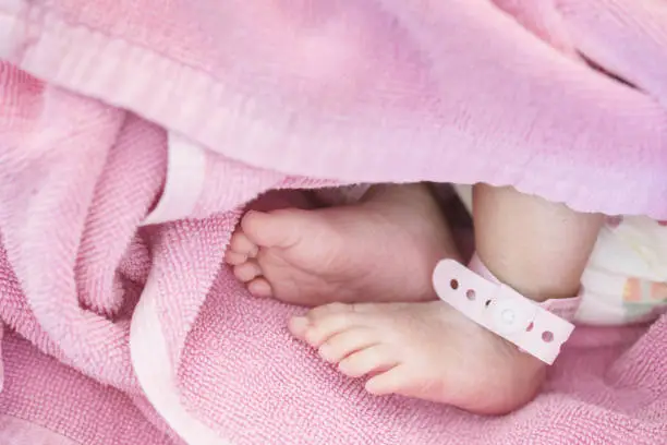 Photo of Closeup foot of baby with newborn ankle tag on bed in hospital textured background