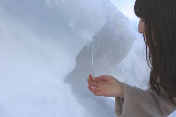 Icicle against light blue sky. Drop of melted snow falls down. Closeup. Illustration about end of winter or beginning of spring. Thaw. Horizontal image.