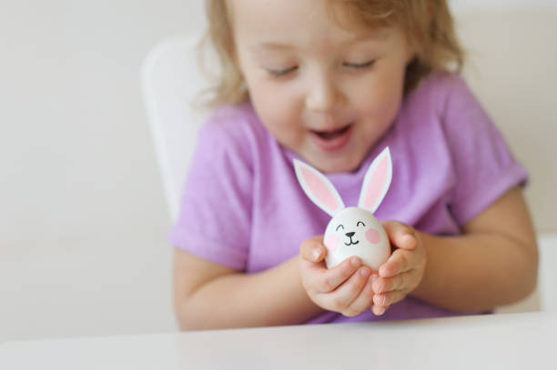 feliz páscoa. a linda garota com orelhas de coelho na mão segura um ovo pequeno - face paint child paint rabbit - fotografias e filmes do acervo