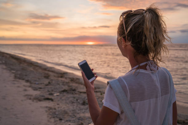 istock Young woman messaging mobile phone at sunset, tropical climate 915109398