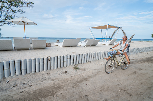 Cheerful young woman on vacations cycling by the beach in the morning, people travel holidays concept.