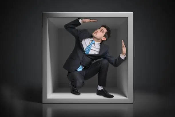 Photo of Young businessman trapped inside uncomfortable small box.