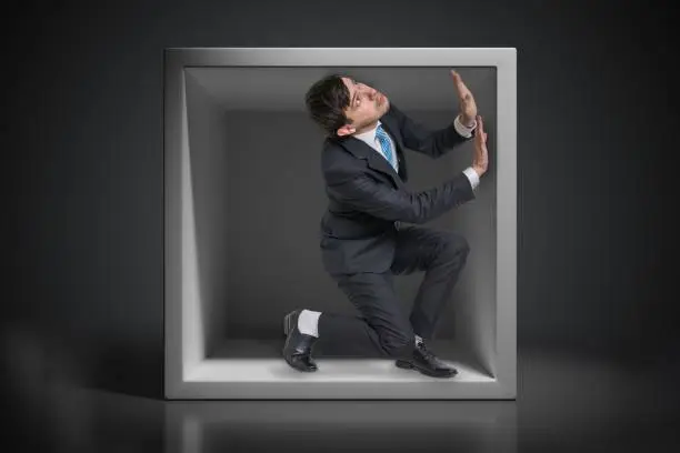 Photo of Young businessman trapped inside uncomfortable small box.