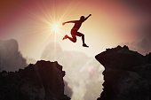 Silhouette of young man jumping over mountains and cliffs at sunset.