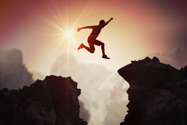 silhouette of young man jumping over mountains and cliffs at sunset. - saltando imagens e fotografias de stock
