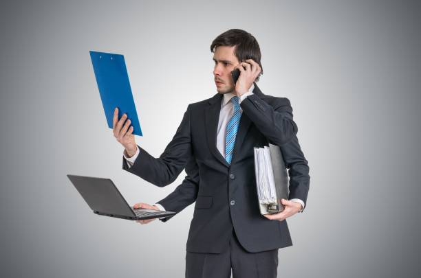 istock Multitasking man at work is calling with phone, reading report, working with laptop and holding office documents. 915116502