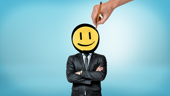 A businessman with crossed hands stands in front view while a giant hand draws a smiley face instead of his head. Business person. Personal brand. Corporate culture.