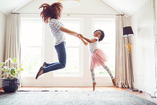 Side view of mother and daughter jumping while performing ballet. Woman and girl are practicing at home. Determined family is dancing against windows.