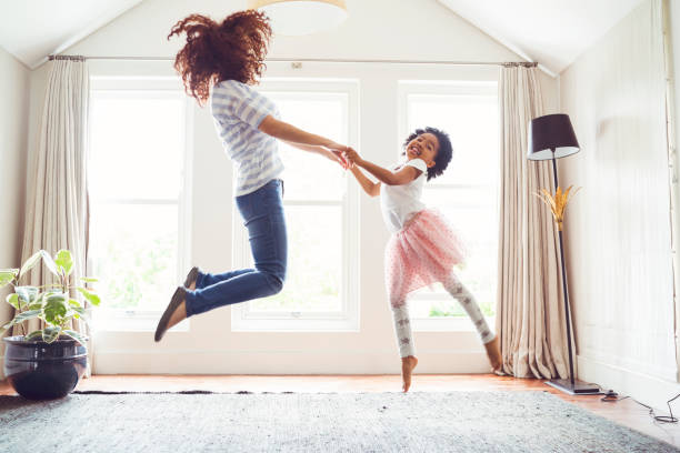 Mother and daughter jumping while doing ballet Side view of mother and daughter jumping while performing ballet. Woman and girl are practicing at home. Determined family is dancing against windows. ballet photos stock pictures, royalty-free photos & images