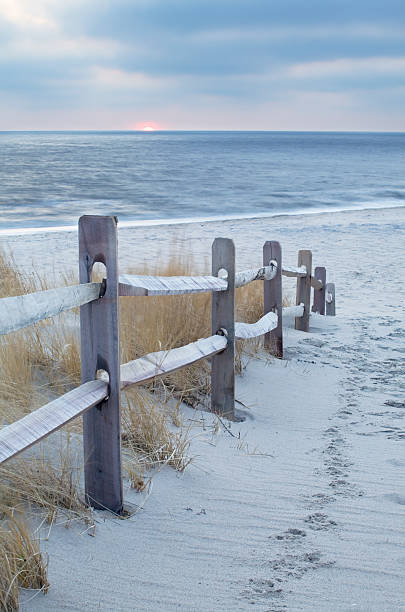 Wooden railing next to sandy path leading to beach stock photo