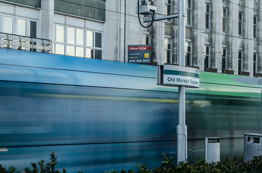 A long exposure of a tram moving past the Old Market Square Nottingham Express Transit sign in Nottingham, England.