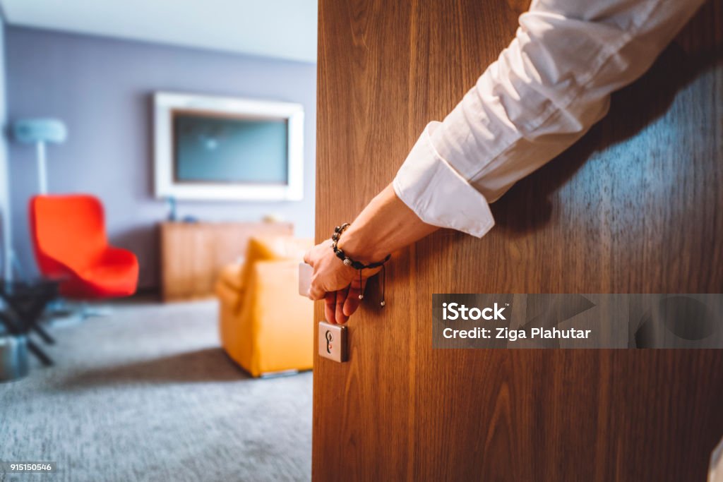 Man hand opening the door of the luxurious hotel room Toned man closing the door of the luxurious hotel room, man wearing a bracelet and a white shirt, closing the wooden door, nice and luxurious hotel room in the background. Door Stock Photo