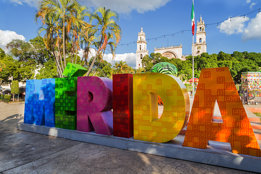 Muestra colorida Mérida con bandera mexicana y la calle de la Catedral. Un parque frente a la señal de Merida en la Plaza Grande en Mérida, México photo