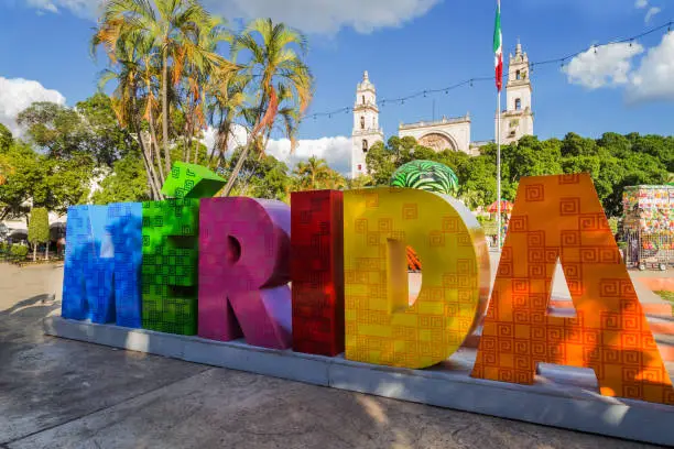 Photo of Colorful sign Merida with mexican flag and cathedral street. A park in front of the Merida sign at the Plaza Grande in Merida, Mexico