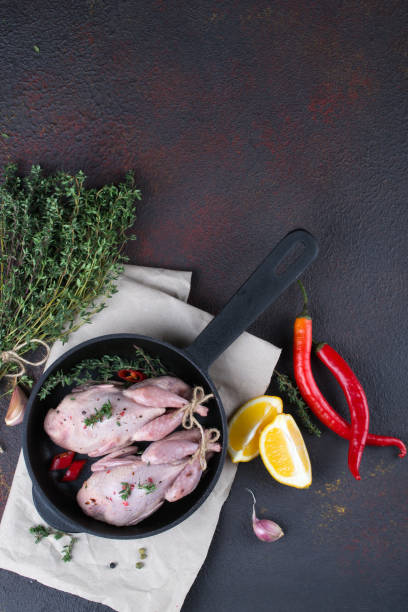 istock Small raw quals with some spice ready for cooking on black round pan . 915156736