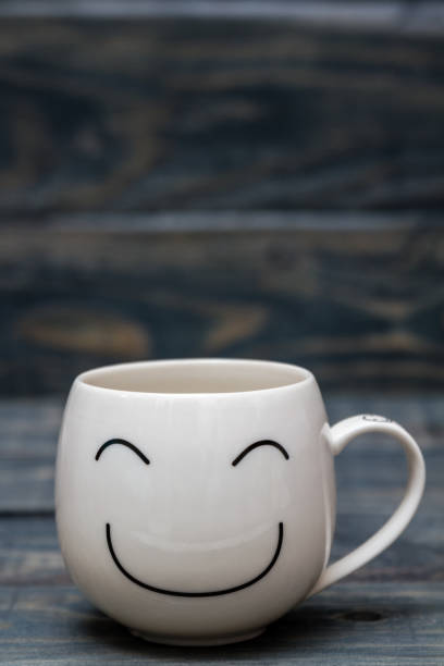 istock White Cup with Smiley Face on Blue Wooden Table 915157538