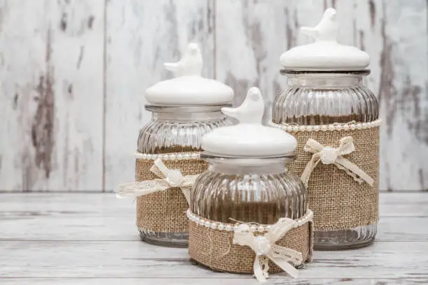 Glass round jars with linens, ribbons and birds on white wooden background