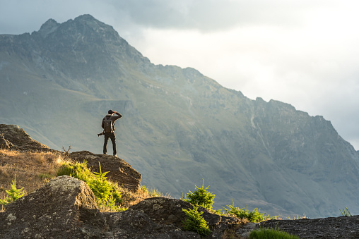 Young male photographer looking at mountain scenery during golden hour sunset in Queenstown, South Island, New Zealand. Travel and photography concept