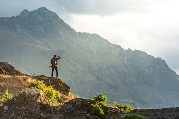 young male photographer looking at mountain scenery during sunset in queenstown, new zealand - nature photographer imagens e fotografias de stock