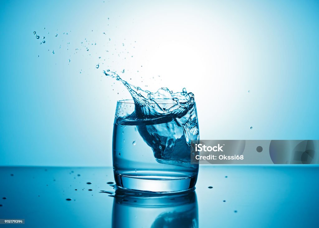 Pure water splashing out of glass Pure water splashing out of glass on blue background Water Stock Photo