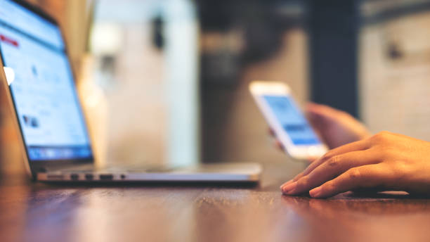 istock woman holding mobile phone while using laptop on wooden table in office 915182520