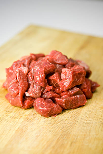 Cubos de carne crua em uma tábua de cortar - foto de acervo