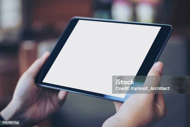 Mockup Image Of Womans Hand Holding Black Tablet Pc With Blank White Screen In Wooden Cafe Stock Photo - Download Image Now