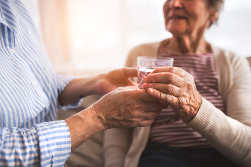 Two unrecognizable senior women at home, holding a glass of water. Family and generations concept.