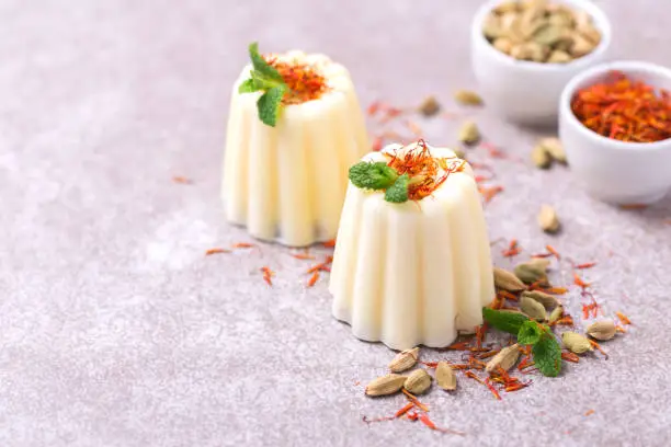 Traditional Rajasthani Indian cuisine. Homemade kulfi dessert, ice cream with safron, mint and nuts on gray slate background. Copyspace, horizontal view.