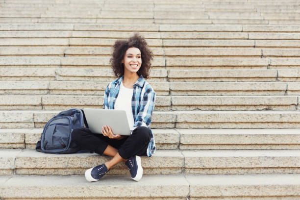 istock Smiling student sitting on stairs using laptop 915202336