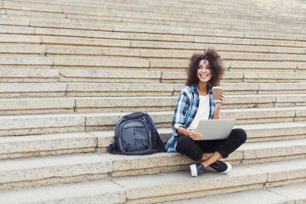 istock Smiling student sitting on stairs using laptop 915202370