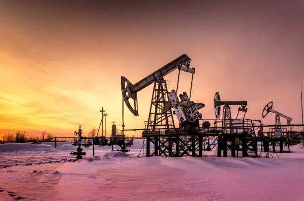 Pump jack, wellhead and pipeline during sunset in the oilfield. Winter period. Oil and gas concept. Toned.