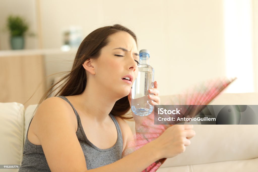 Girl suffering a heatstroke refreshing with a fan Stressed girl suffering a heatstroke refreshing with a fan sitting on a couch in the living room at home Heat - Temperature Stock Photo