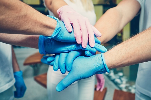 Teamwork of the doctors in hospital. Hands of three men in blue gloves and one woman in pink gloves. Themes health care, cooperation, trust and success.