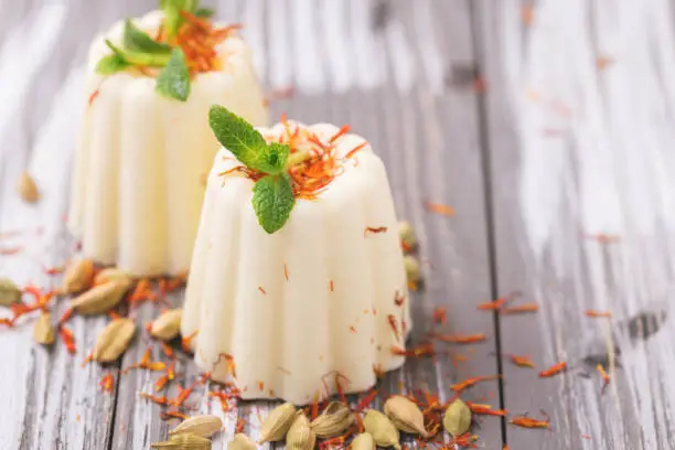 Traditional Rajasthani Indian cuisine. Homemade kulfi dessert, ice cream with safron, mint and nuts on gray wooden background. Copyspace, horizontal view.