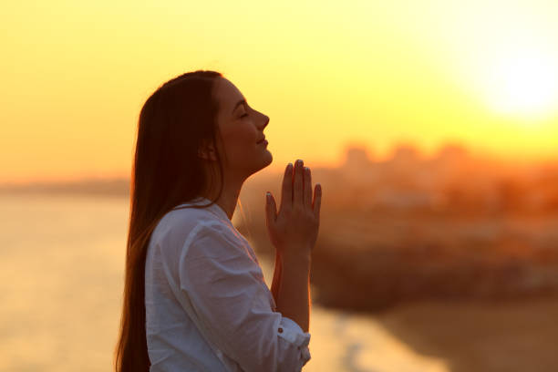 Profile of a woman praying at sunset Side view backlight portrait of a woman praying and looking above at sunset pleading photos stock pictures, royalty-free photos & images
