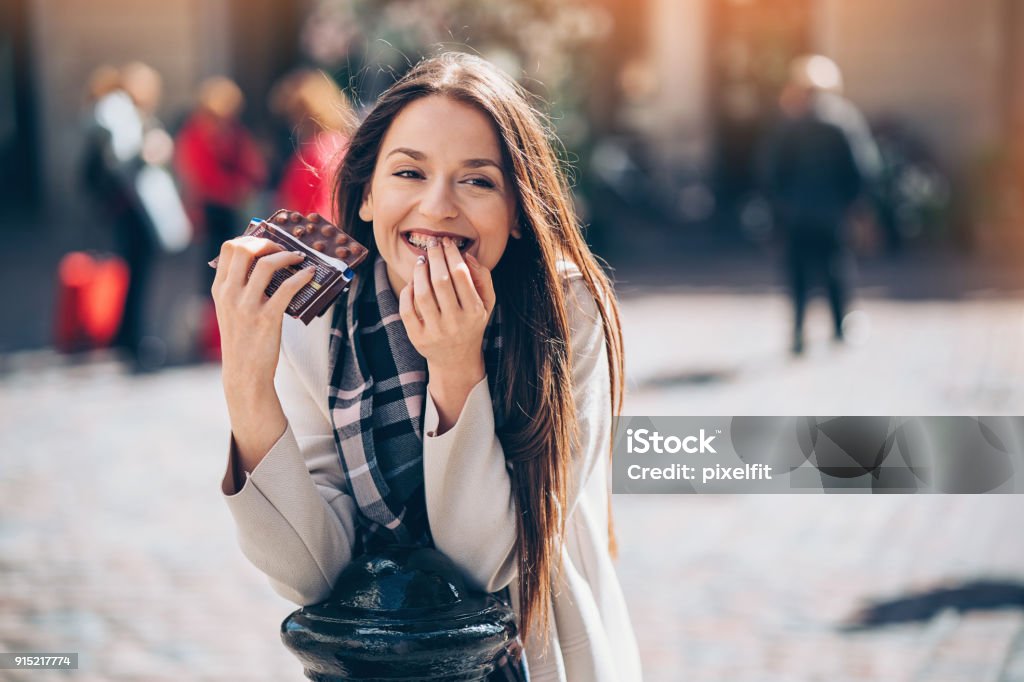 Guilty pleasures Smiling young businesswoman eating chocolate outdoors in the city Chocolate Stock Photo