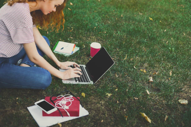 istock Young redhead girl in casual using laptop sitting under a tree 915218342