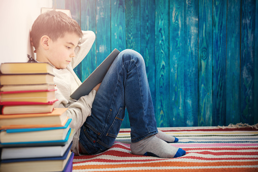 eight years old child reading a book at home. Boy studying on blue background