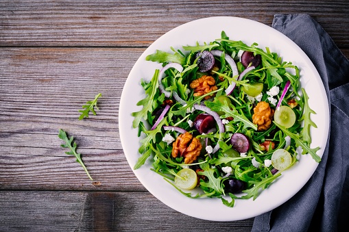 green salad bowl with arugula, walnuts, goat cheese, red onion and grapes on wooden background