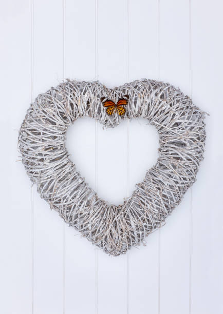 Wicker heart shaped wreath on wooden background decorated with a butterfly