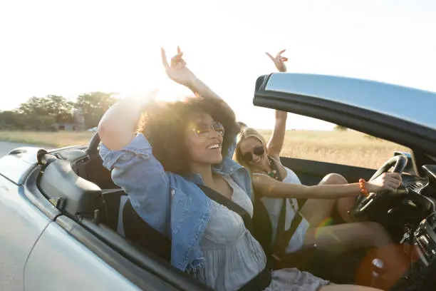 Young women singing and having fun on road trip with convertible car.