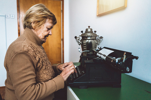 A beautiful old woman typing on a typewriter. They are very uncommon nowadays.