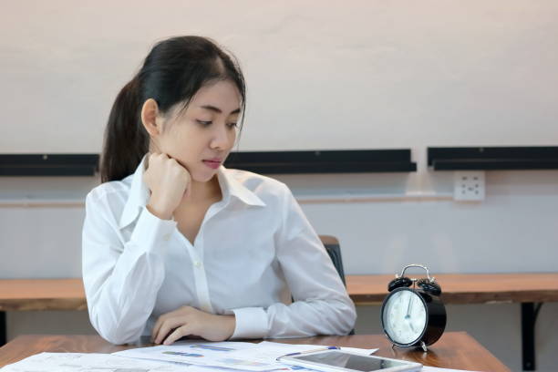 atrakcyjna młoda azjatycka kobieta biznesu patrząc na zegar w miejscu pracy w biurze. - waiting women clock boredom zdjęcia i obrazy z banku zdjęć