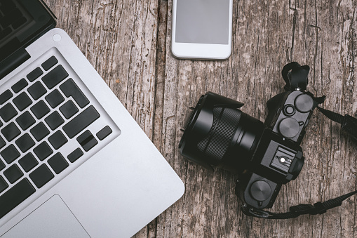 Laptop, white smartphone and retro camera on an old wooden textured desk. Technology concept.