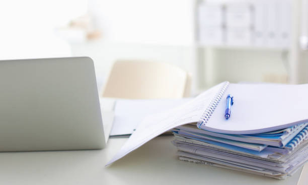 istock Laptop with stack of folders on table on white background 915279882