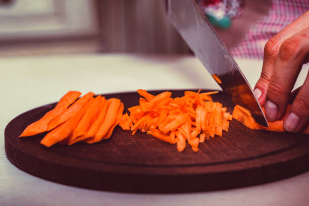 istock Woman's hands slice carrot on wooden board 915281268